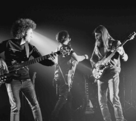 Three band members performing on a stage in black and white