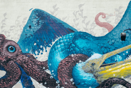 Mural on the side of a building with two octopuses and a stork embraced in battle