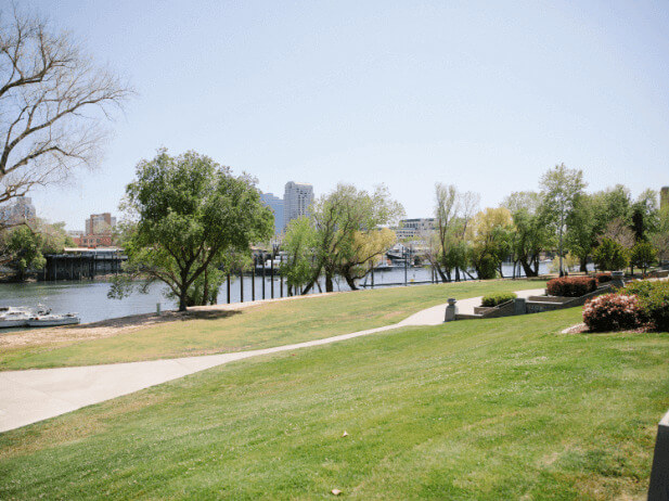 A walking path along next to the Sacramento River with a view of the city in the background
