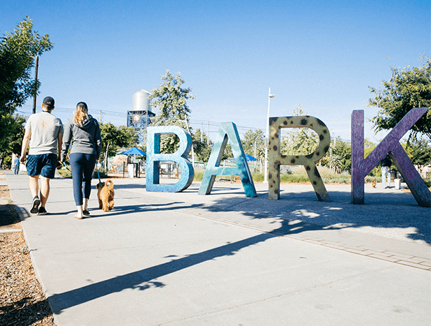 A woman walking her dog in a local dog park in Sacramento, California next to large BARK sign