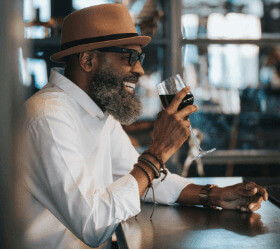 An older man with beard, sunglasses and tan fedora drinking a glass of red wine in downtown Sacramento, California