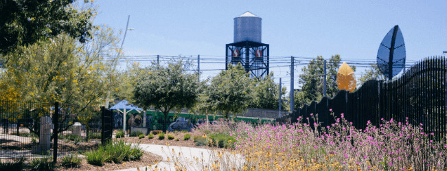 A water tower in the background of a public park with bike path and flowers