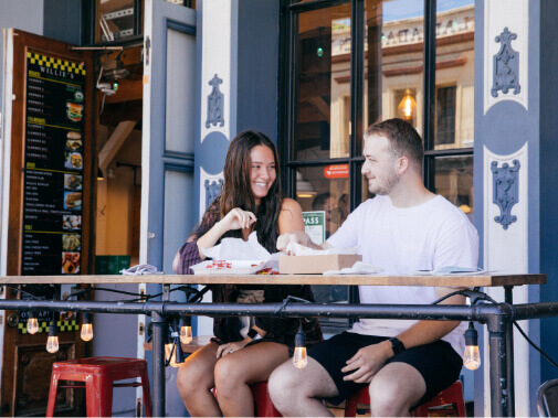 A young couple sitting outside at a restaurant patio eating lunch and laughing