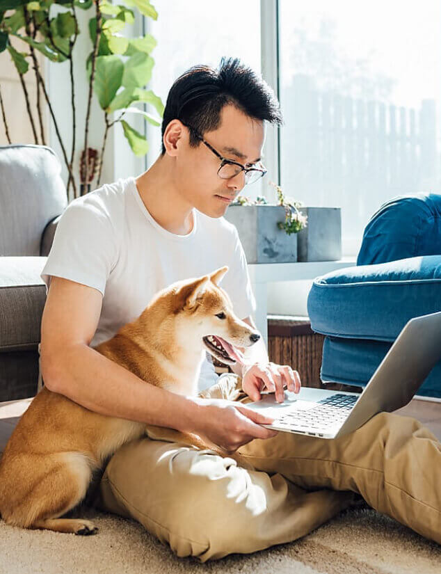 A millennial man working from home sitting on his living room floor with his Shiba dog