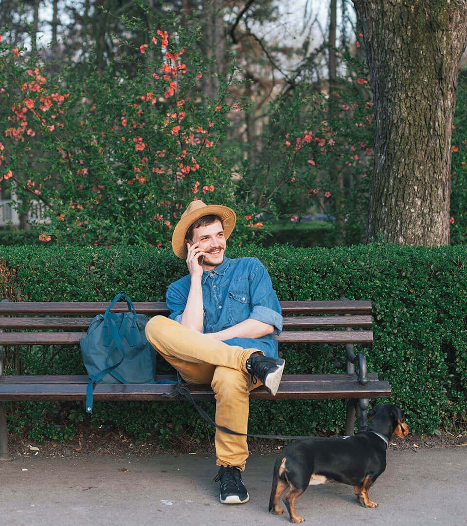 A man talking on the phone while sitting on a bench with his dog