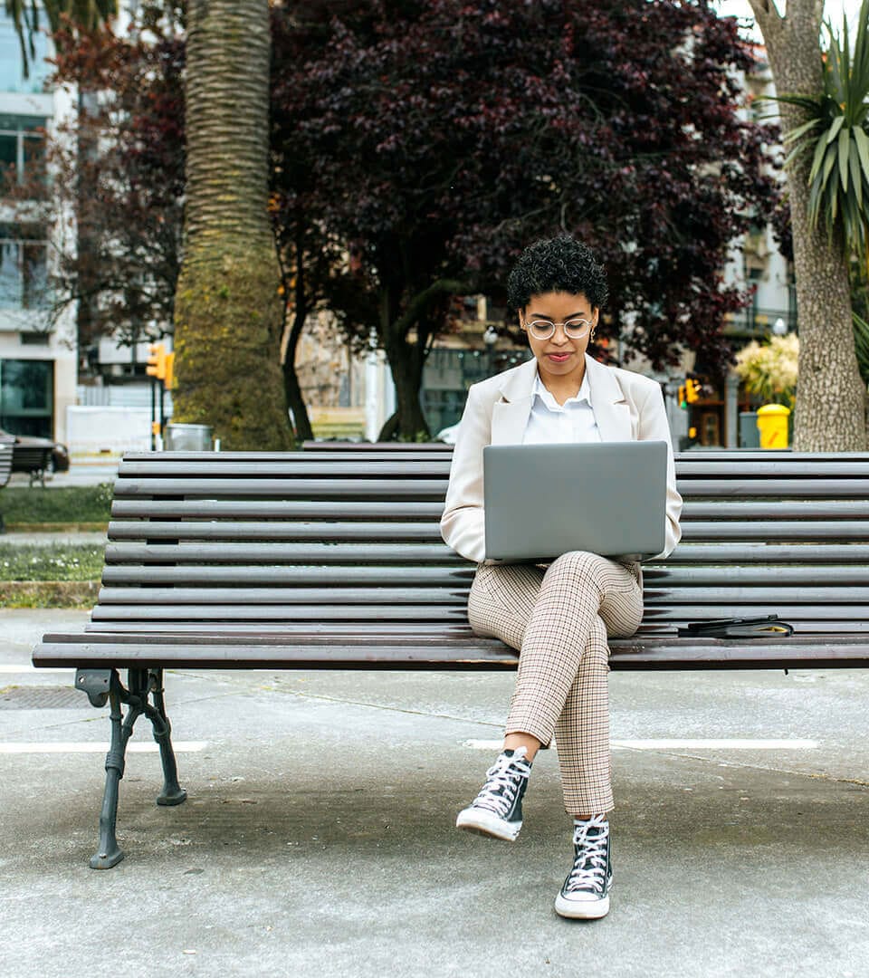 A woman working on a laptop while sitting on a bench