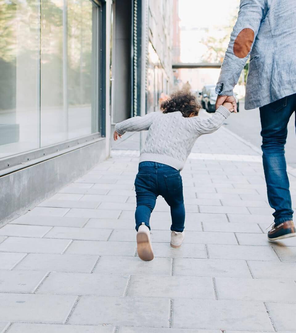 A young child holding their parents hand while walking along a sidewalk