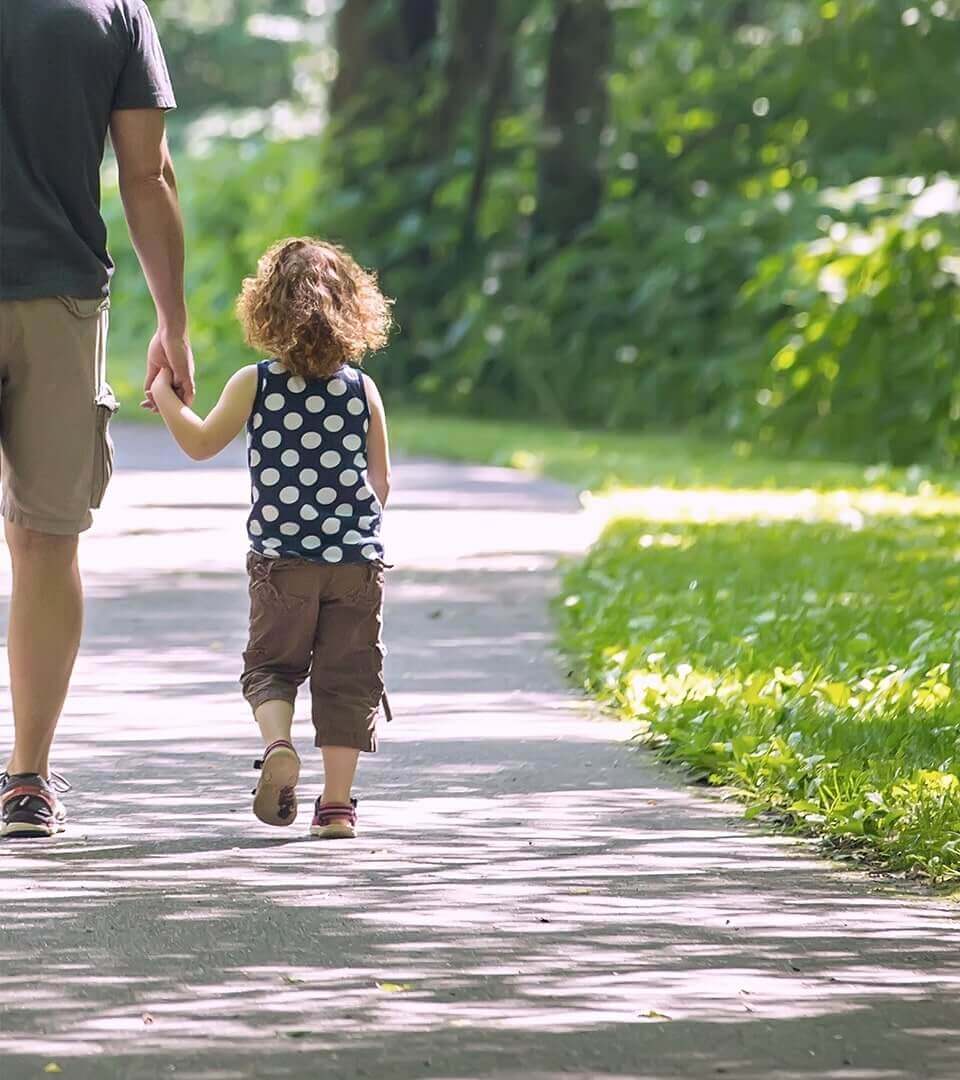 A young child holding their parents hand while walking along a path through a park