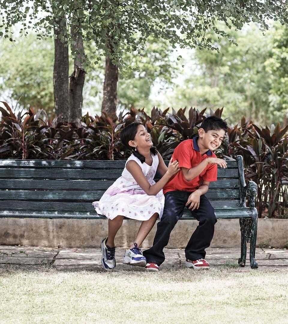 A young boy and girl laughing while sitting on a bench in a park