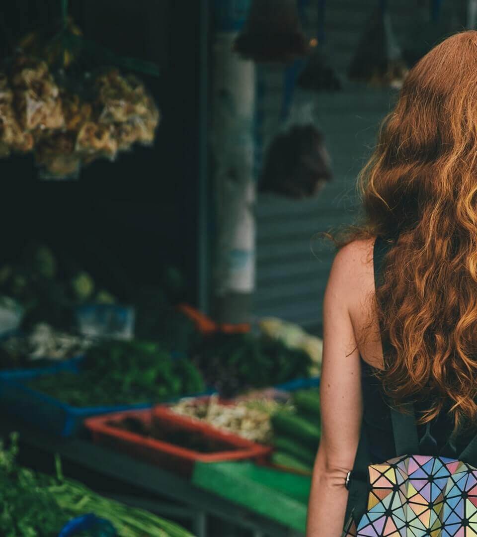 View from behind of a woman with long red hair walking through a farmer's market