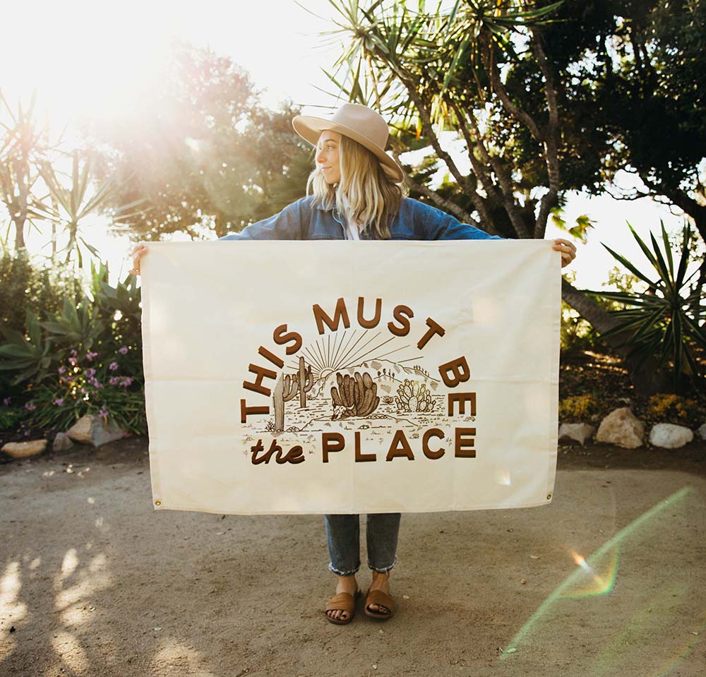 A young woman holding a woven blanket that says This Must Be The Place